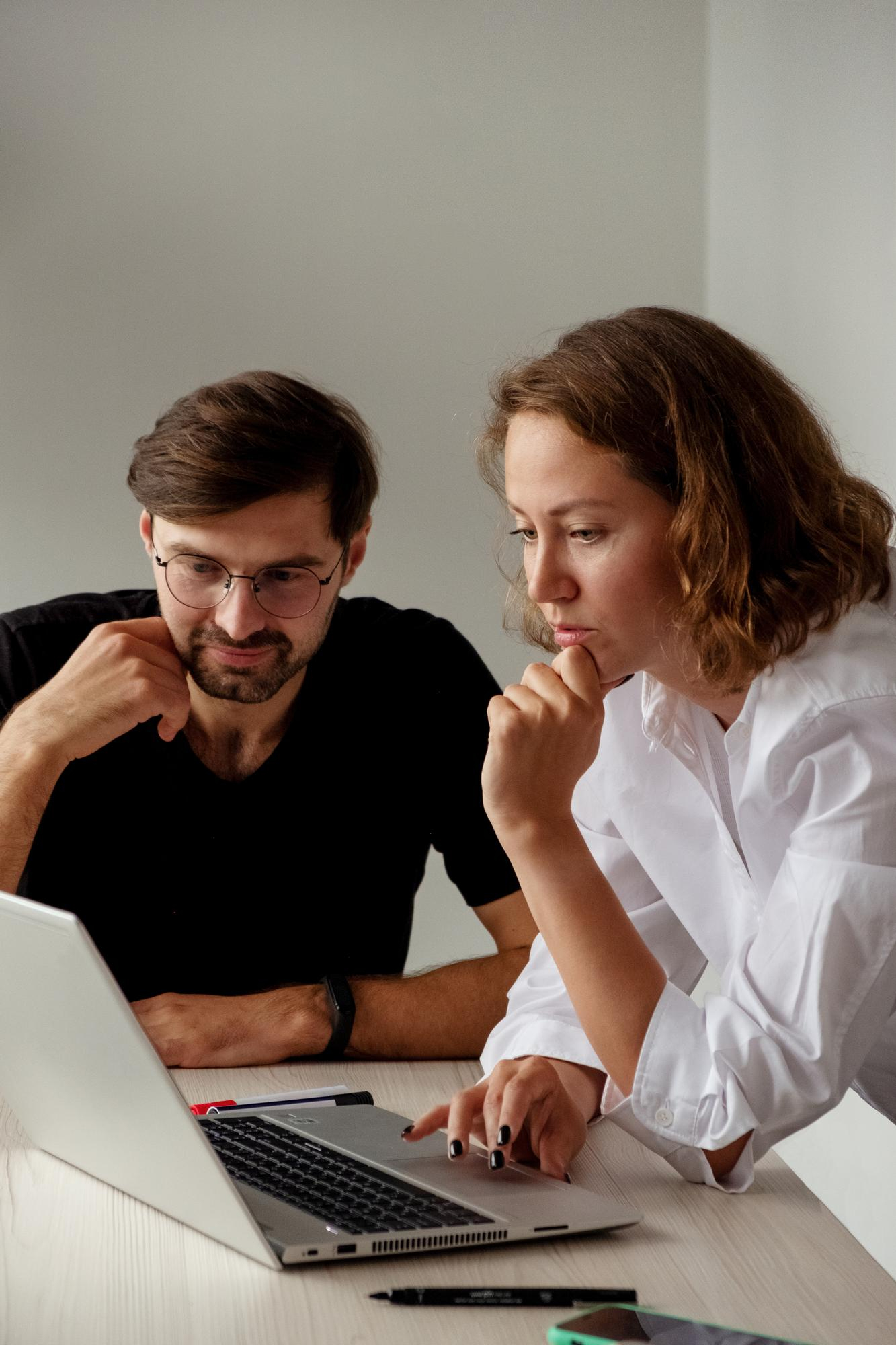Two professionals reviewing project details on a laptop, representing a flexible time and material engagement model for evolving software development requirements.