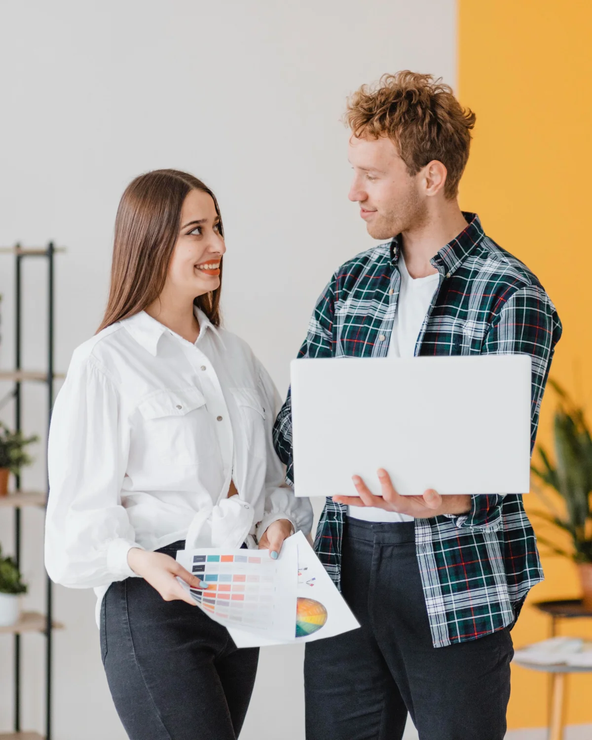 A woman holding design charts and a man holding a laptop, discussing custom platform specs and native payment feature integration.